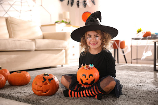 Cute little girl with pumpkin candy bucket wearing Halloween costume at home